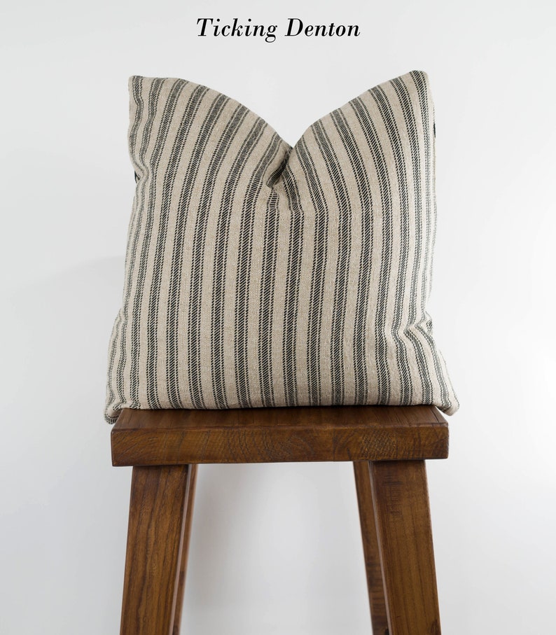 May include: A black and white striped pillow on a wooden stool. The pillow is made of ticking fabric and has a simple, farmhouse style.
