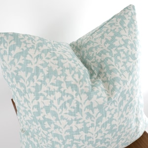 May include: A light blue throw pillow with a white floral pattern. The pillow is made of a soft, textured fabric.