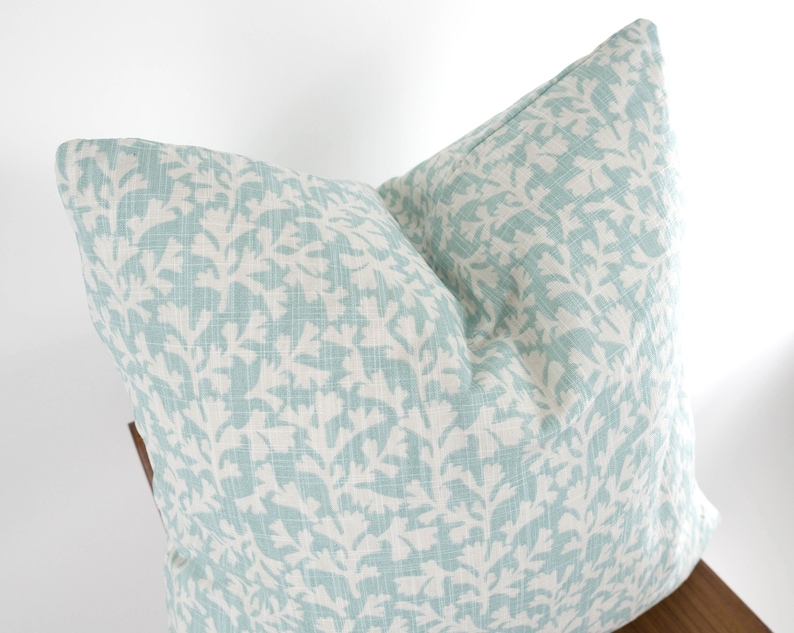May include: A light blue throw pillow with a white floral pattern. The pillow is made of a soft, textured fabric.