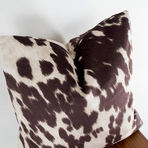 May include: A brown and white patterned throw pillow with a cowhide print.