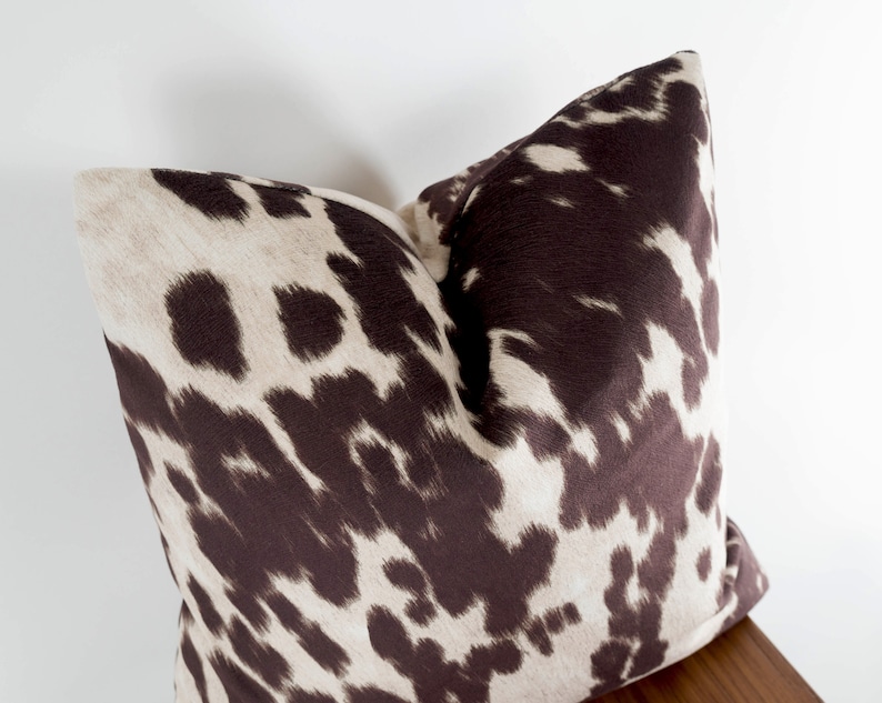 May include: A brown and white patterned throw pillow with a cowhide print.