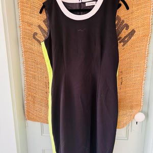 May include: Sleeveless black dress with a white neckline and a neon yellow side panel. The dress is hanging on a black hanger. The Calvin Klein logo is visible on the dress.