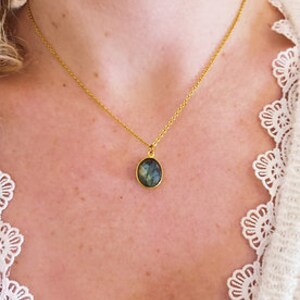 Può includere: Una collana con catena dorata con un ciondolo ovale in labradorite, con sfumature di verde e blu.
