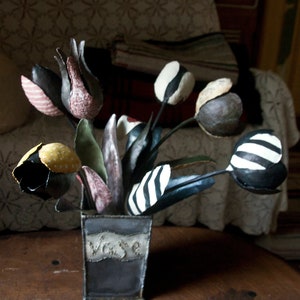 May include: A bouquet of black and white striped, polka dot, and patterned fabric tulips in a gray metal vase with the word "Vase" written on the side.
