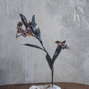 Könnte beinhalten: Eine Metallskulptur einer Blume mit schwarzen Stielen und Blättern und kupferfarbenen Blüten. Die Skulptur steht auf einem weißen Steinsockel.