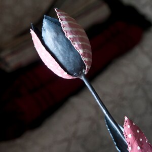 May include: A pink and white striped metal tulip with a black stem. The tulip is painted with white polka dots.
