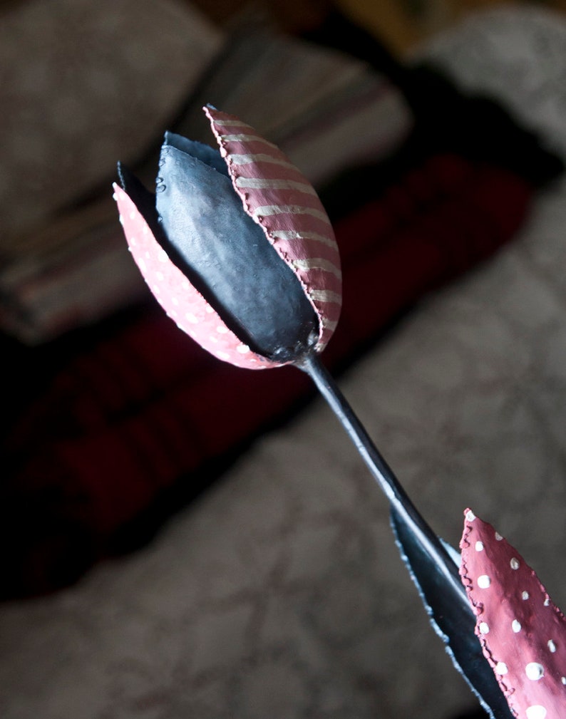 May include: A pink and white striped metal tulip with a black stem. The tulip is painted with white polka dots.