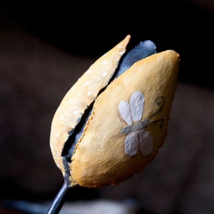 May include: A yellow metal tulip with a white butterfly painted on it. The tulip has white polka dots and a black stem.