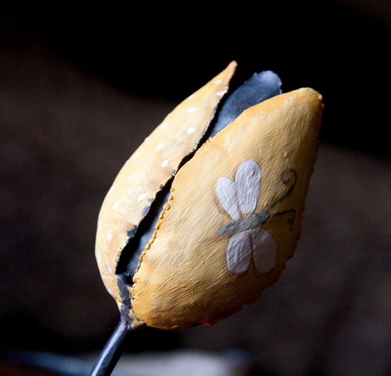 May include: A yellow metal tulip with a white butterfly painted on it. The tulip has white polka dots and a black stem.