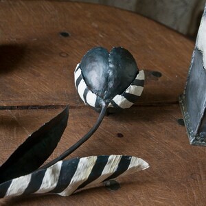 May include: Three black and white striped metal tulips with black stems. The tulips are sitting on a wooden surface.