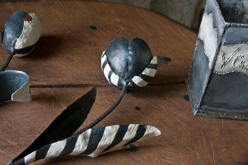May include: Three black and white striped metal tulips with black stems. The tulips are sitting on a wooden surface.