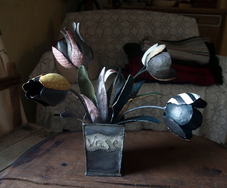 May include: A bouquet of black, white, and yellow fabric tulips in a metal vase with the word "Vase" written on the front.