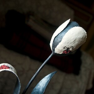 May include: A black metal sculpture of a tulip with white paint and red ladybug accents.