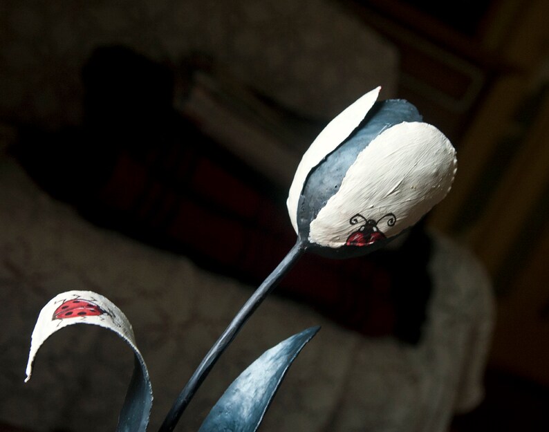 May include: A black metal sculpture of a tulip with white paint and red ladybug accents.