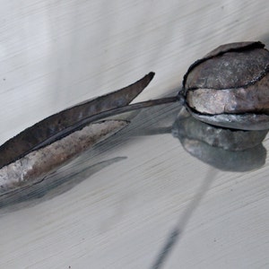 Op de afbeelding: Een metalen sculptuur van een tulp met een zilveren afwerking. Het beeld is gemaakt van dunne metalen platen die aan elkaar zijn gelast om de vorm van een tulp te cre&euml;ren.