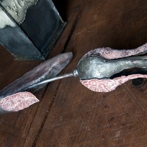 May include: A metal tulip sculpture with a silver and pink finish. The tulip is made of multiple pieces of metal that have been joined together to create a realistic shape. The tulip has a delicate, intricate design.