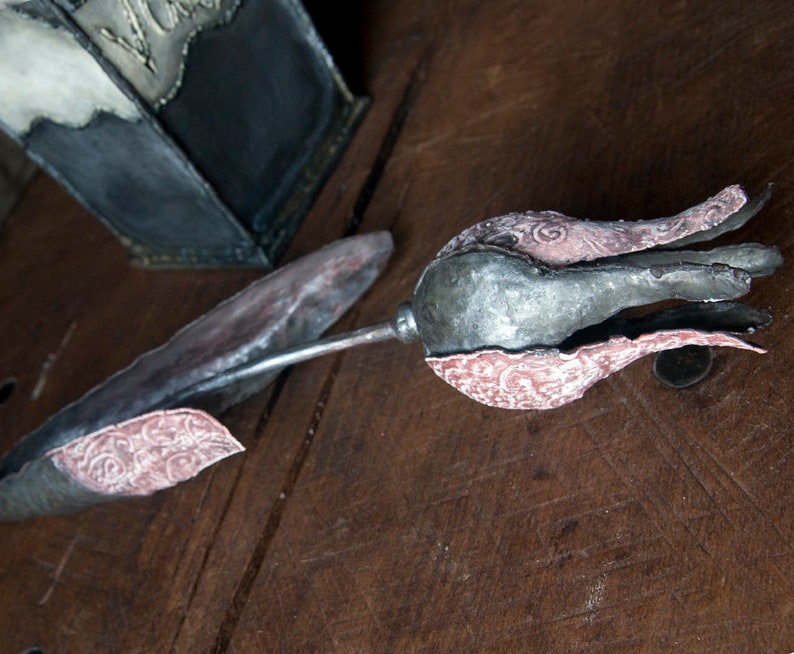 May include: A metal tulip sculpture with a silver and pink finish. The tulip is made of multiple pieces of metal that have been joined together to create a realistic shape. The tulip has a delicate, intricate design.