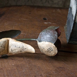 May include: A gray and white flower made of paper with musical notes printed on it. The flower is lying on a wooden surface.