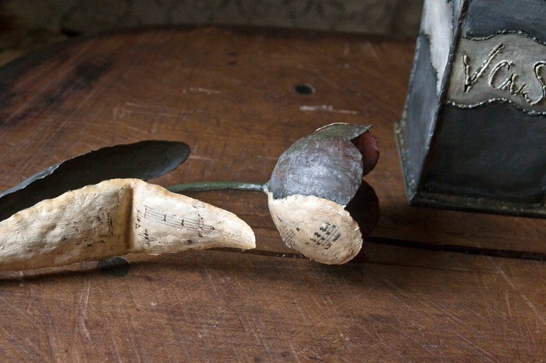 May include: A gray and white flower made of paper with musical notes printed on it. The flower is lying on a wooden surface.