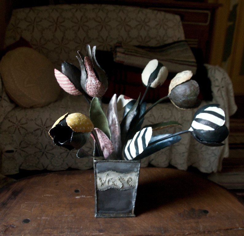 May include: A bouquet of black and white striped, polka dot, and patterned fabric tulips in a gray metal vase with the word "Vase" written on the side.