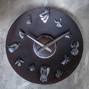 May include: A circular clock with a dark brown metal face and silver hands. The clock face is decorated with twelve small, silver angel figures.