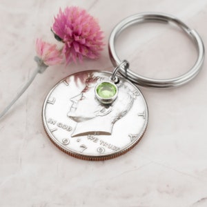 May include: Silver dollar keychain with a green gemstone charm. The coin is dated 1979 and reads "In God We Trust".