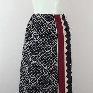 May include: A long black skirt with a geometric pattern in white and a burgundy stripe down the side. The skirt has a black and white trim at the bottom.