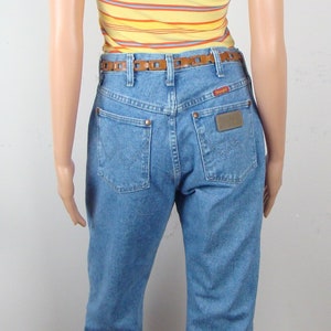 May include: A mannequin wearing a yellow striped t-shirt, light blue jeans, and a brown belt. The jeans have a Wrangler label on the back pocket. The t-shirt has horizontal stripes in orange, purple, and blue.