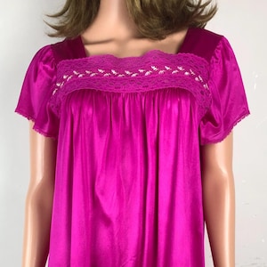 May include: A vibrant fuchsia-colored nightgown with a square neckline and short sleeves. The bodice features a delicate white lace trim. The knee-length dress is made of a smooth, silky fabric, offering a classic and comfortable sleepwear option.