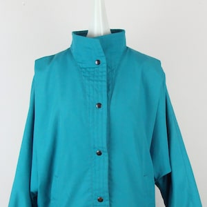 May include: A teal blue jacket with a button-up front and long sleeves. The jacket has a high collar and a slightly oversized fit.