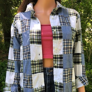 May include: A long-sleeve button-down shirt featuring a patchwork design composed of alternating squares of solid white fabric, solid light blue denim, and a plaid pattern in shades of blue, black, white, and yellow, with a classic collar and front buttons.