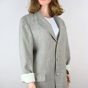 May include: A gray blazer with a subtle striped pattern. The blazer has a single-breasted closure with two buttons and a flap pocket on the left side.