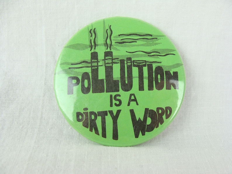 May include: Green button with black text that reads "Pollution is a dirty word". The button features a graphic of two smokestacks with smoke coming out of them.