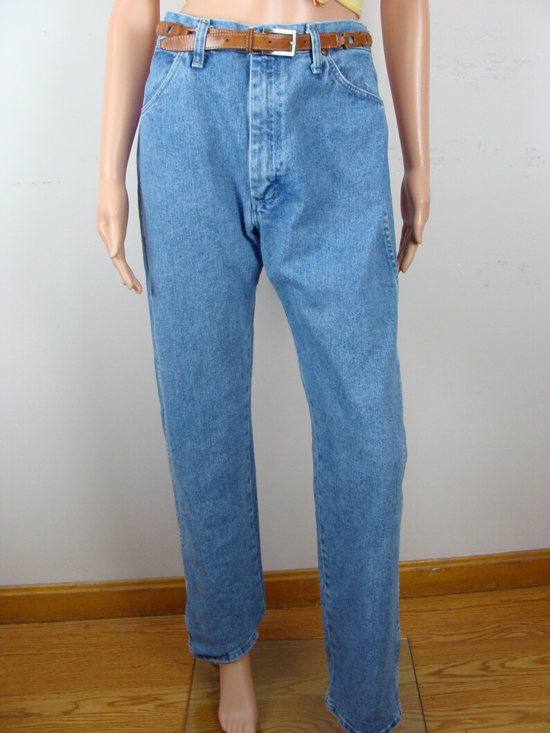 May include: Light blue denim jeans with a brown leather belt. The jeans have a classic five-pocket design and a straight leg cut. The belt has a silver buckle and a series of decorative cutouts.