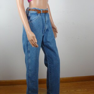 May include: Light blue denim jeans with a brown leather belt. The jeans have a classic five-pocket design and a straight leg fit. The belt is a medium brown color with a rectangular buckle. The jeans are displayed on a mannequin.