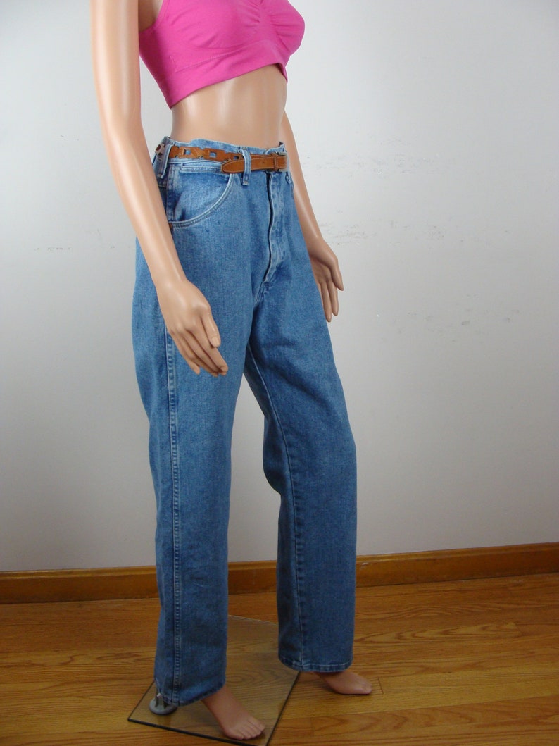 May include: Light blue denim jeans with a brown leather belt. The jeans have a classic five-pocket design and a straight leg fit. The belt is a medium brown color with a rectangular buckle. The jeans are displayed on a mannequin.