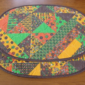 May include: Two brown quilted oval placemats with a patchwork design of orange, green, and brown fabric with floral patterns.
