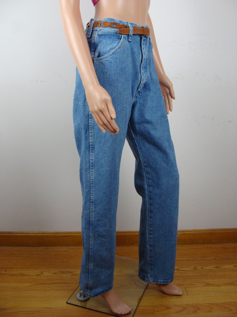 May include: Light blue denim jeans with a brown leather belt. The jeans have a classic straight-leg fit and a traditional five-pocket design. The belt is a medium brown color with a decorative cut-out pattern.