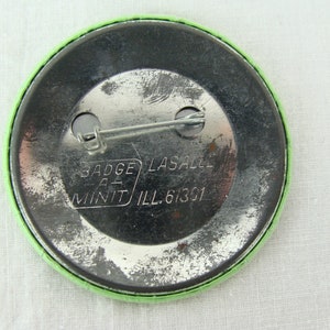 May include: The back of a green button with a silver pin and the text "Badge-A-Mint LaSalle Ill. 61301"