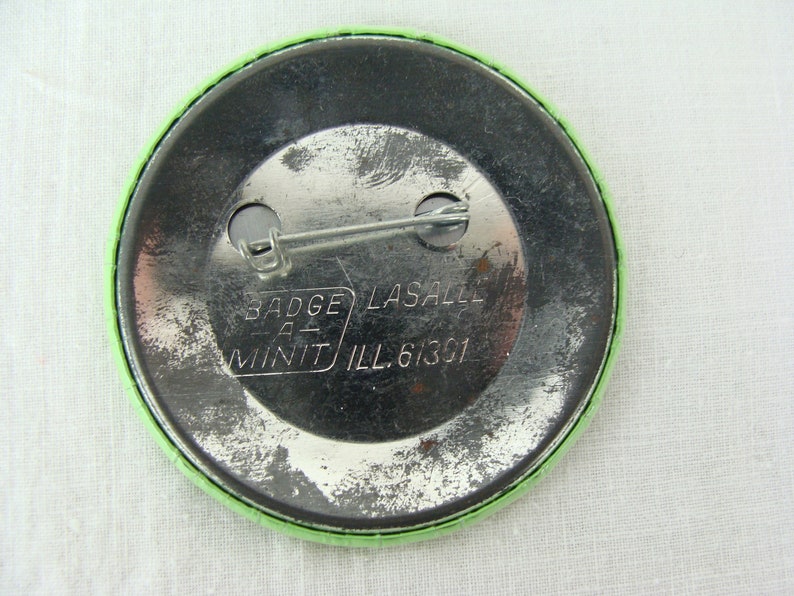 May include: The back of a green button with a silver pin and the text "Badge-A-Mint LaSalle Ill. 61301"