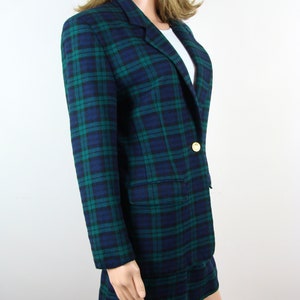 Op de afbeelding: Een blauwe en groene geruite blazer met een enkele gouden knoop. De blazer is gemaakt van een zachte, geweven stof.
