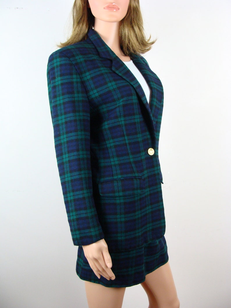 Op de afbeelding: Een blauwe en groene geruite blazer met een enkele gouden knoop. De blazer is gemaakt van een zachte, geweven stof.