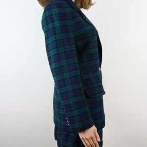Op de afbeelding: Een blauwe en groene geruite blazer en rok set. De blazer heeft een reverskraag, lange mouwen en twee steekzakken. De rok is A-lijn en valt boven de knie.