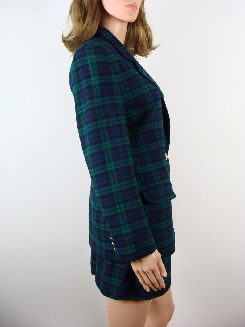 Op de afbeelding: Een blauwe en groene geruite blazer en rok set. De blazer heeft een reverskraag, lange mouwen en twee steekzakken. De rok is A-lijn en valt boven de knie.