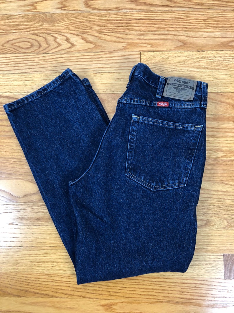 May include: A pair of dark blue denim jeans with a Wrangler label on the back pocket. The jeans have a classic straight leg style.