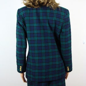 Op de afbeelding: Een blauwe en groene geruite blazer en rok set. De blazer heeft gouden knopen aan de manchetten. De rok is een minirok.