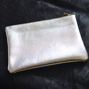 May include: A silver leather clutch with a zipper closure.