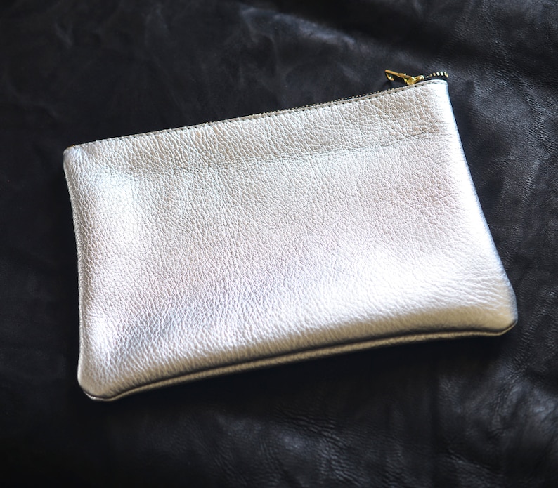 May include: A silver leather clutch with a zipper closure.