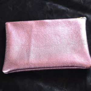 May include: A pink metallic leather clutch purse with a zipper closure.