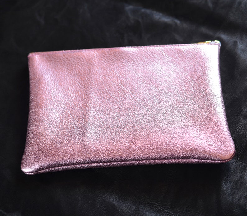 May include: A pink metallic leather clutch purse with a zipper closure.